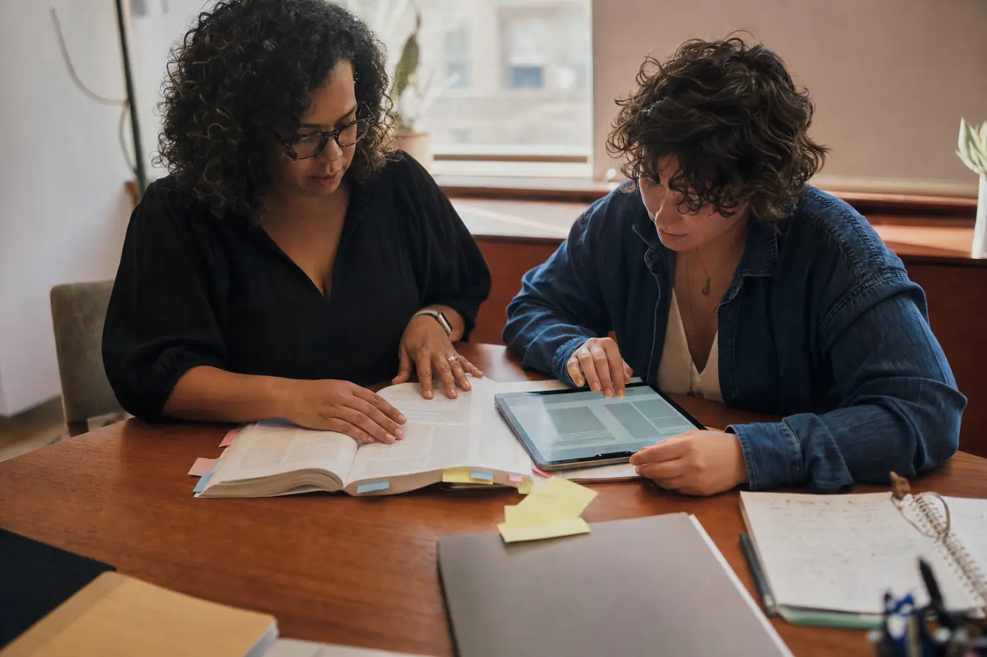 Two editors comparing a printed textbook against the same content on a tablet
