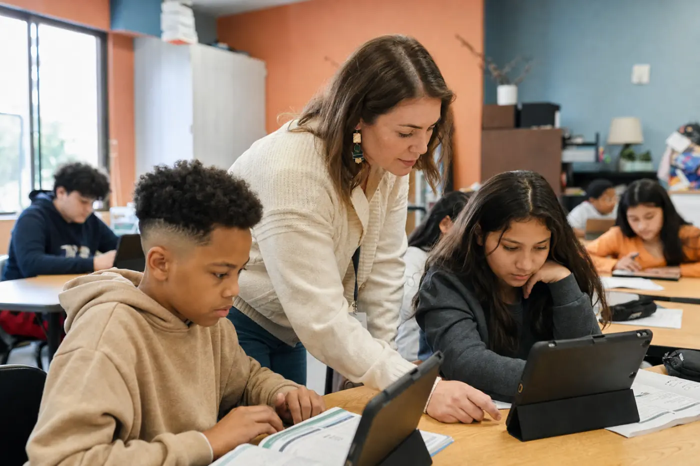 A teacher helping two students working from tablets in a classroom