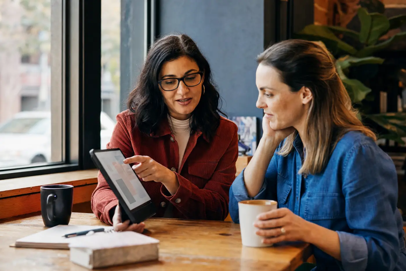 One professional showing another something on a tablet at a cafe table