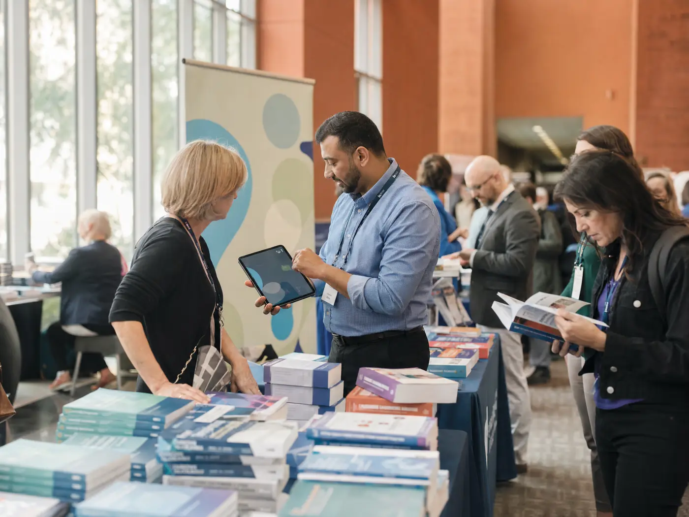 An association's conference bookstore, with a staff member showing an attendee a title on a tablet